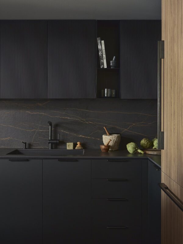 Modern black kitchen renovation with ribbed cabinetry and natural stone backsplash in Toronto.