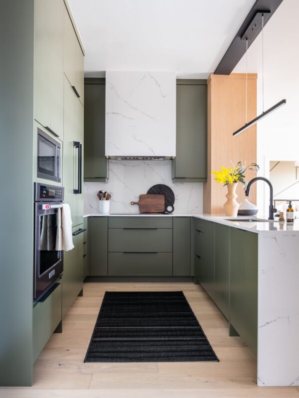 Modern green galley kitchen with waterfall quartz island and integrated appliances.